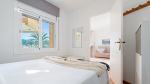 A bedroom with a large bed, a window with a view of palm trees, a door leading to another room, and a small balcony. - CYE V LA PINEDA (La Pineda)