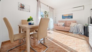 A modern living room with a dining area, featuring a wooden table, beige chairs, a pink sofa, and a large window with sheer curtains. - CYE V LA PINEDA (La Pineda)