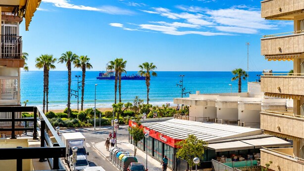 Vista sulla costa con una nave blu, palme e un edificio con un cartello rosso.
