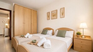 Una camera d'albergo con due letti, un armadio in legno, un comodino con una lampada e decorazioni alle pareti.