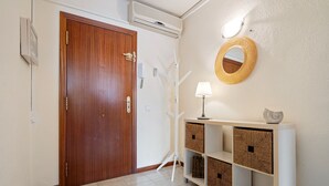 Un corridoio con una porta in legno, un tavolino consolle bianco con cesti, uno specchio fissato alla parete e un pavimento con motivo geometrico.