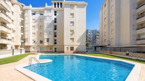 En swimmingpool omgiven av ett stenbelagt område, med en flervåningsbostadsbyggnad i bakgrunden.