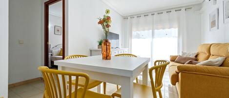 A living room with a white table and yellow chairs, a sofa, and a vase with flowers.