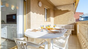 A sunlit outdoor dining area with white tables and chairs, a glass door leading to a kitchen, and a stone wall. - ALBENIZ Superior (La Pineda)