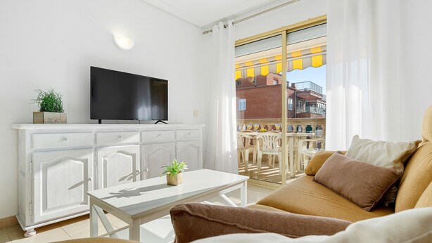 A modern living room with a flat-screen TV, a white cabinet, a dining table, and a sofa with cushions. - ALBENIZ Superior (La Pineda)