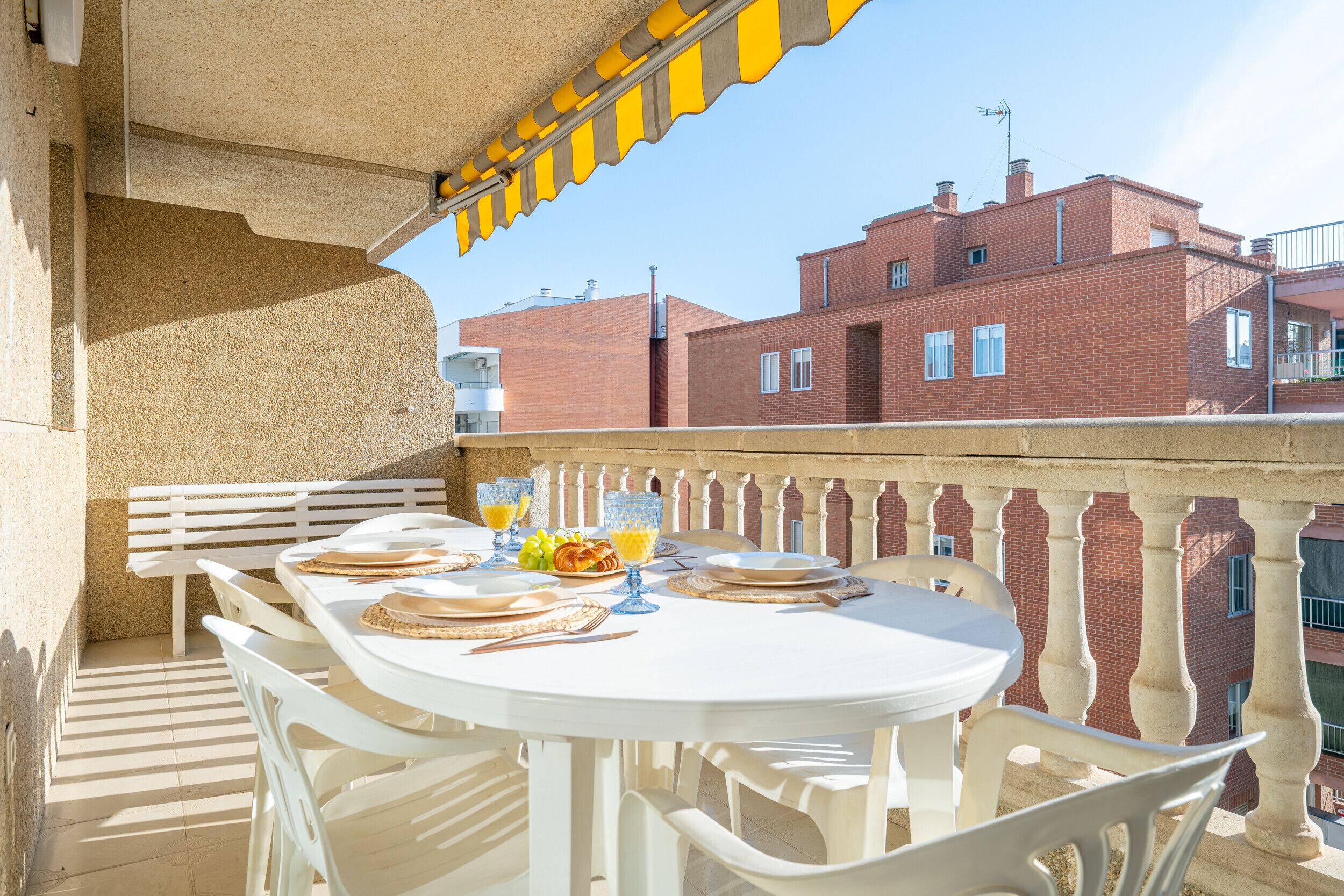 A balcony with a white table set for dining, overlooking a red brick building.
