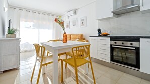 A modern kitchen with white cabinetry, a built-in oven, and a dining area with a white table and yellow chairs. - ALBENIZ Superior (La Pineda)