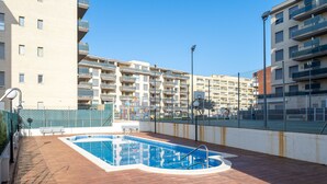 A rooftop pool with a wooden deck, surrounded by a high fence, and adjacent to multi-story residential buildings. - ALBENIZ Superior (La Pineda)