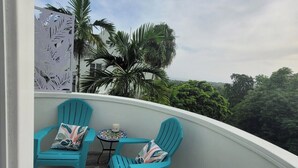 A balcony with two turquoise chairs and a small round table, surrounded by a white wall and a decorative panel. - Peaceful Hillside Retreat with Pool. (Ocho Rios)