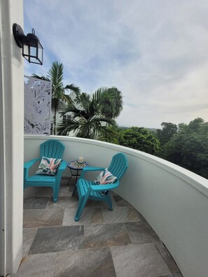 A balcony with two turquoise chairs and a small round table, surrounded by a white wall and a decorative panel. - Peaceful Hillside Retreat with Pool. (Ocho Rios)