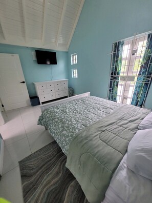A bedroom with a bed, a dresser, a television, and a window with curtains.