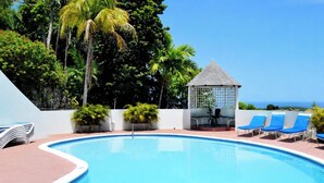 A swimming pool with lounge chairs and a gazebo, surrounded by tropical vegetation. - Peaceful Hillside Retreat with Pool. (Ocho Rios)