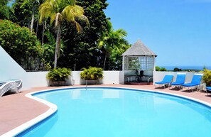 A swimming pool with lounge chairs and a gazebo, surrounded by tropical vegetation. - Peaceful Hillside Retreat with Pool. (Ocho Rios)