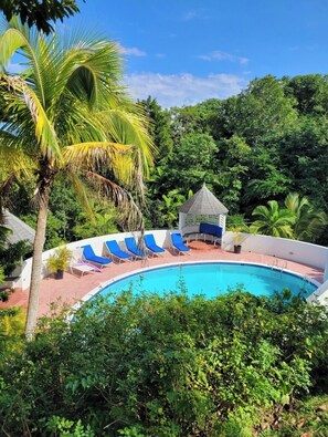 A swimming pool with lounge chairs and a gazebo surrounded by lush greenery.