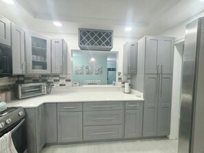 A modern kitchen with grey cabinets, a built-in oven, and a stainless steel refrigerator.