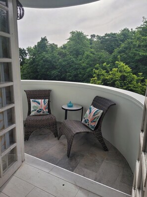 A balcony with two wicker chairs and a small round table, overlooking a lush green forest.
