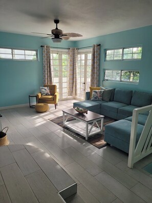 Quarto com sofá azul, poltrona amarela, mesa de centro branca e ventilador de teto.