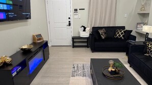 Een moderne woonkamer met een flatscreen televisie, zwarte banken, een salontafel en een klein bijzettafeltje.