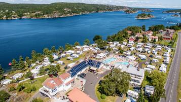 An aerial view of a campground with RVs, a swimming pool, and a large building with solar panels.