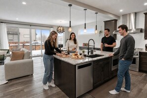 A modern kitchen with a central island, stainless steel appliances, and pendant lighting. - Luxury Group Home • Karaoke, Games & Sleeps 14 (Calgary)
