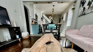 Une longue table à manger en bois naturel, dans un salon moderne agrémenté d’un canapé et d’un téléviseur.