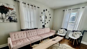 Un salon avec un canapé rose, une table basse en bois, un fauteuil blanc et un tapis.