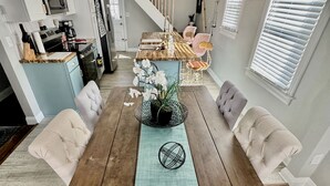 Un espace repas comprenant une table en bois, des chaises rembourrées, un luminaire suspendu et un escalier menant à une autre pièce.