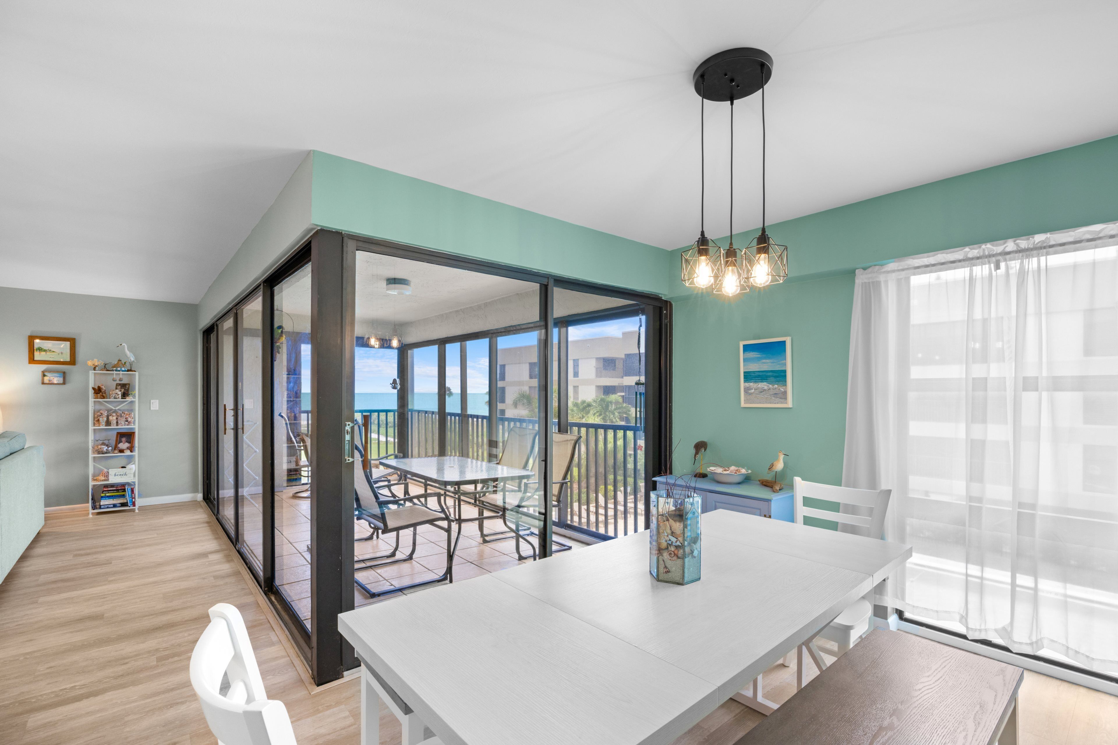 Un espace de vie à aire ouverte comprenant une table à manger, des chaises, une bibliothèque et une vue sur un balcon extérieur, accessible par une porte vitrée.