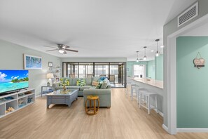 Una sala de estar moderna con televisor, sofá, mesa de centro y un comedor con taburetes de bar.