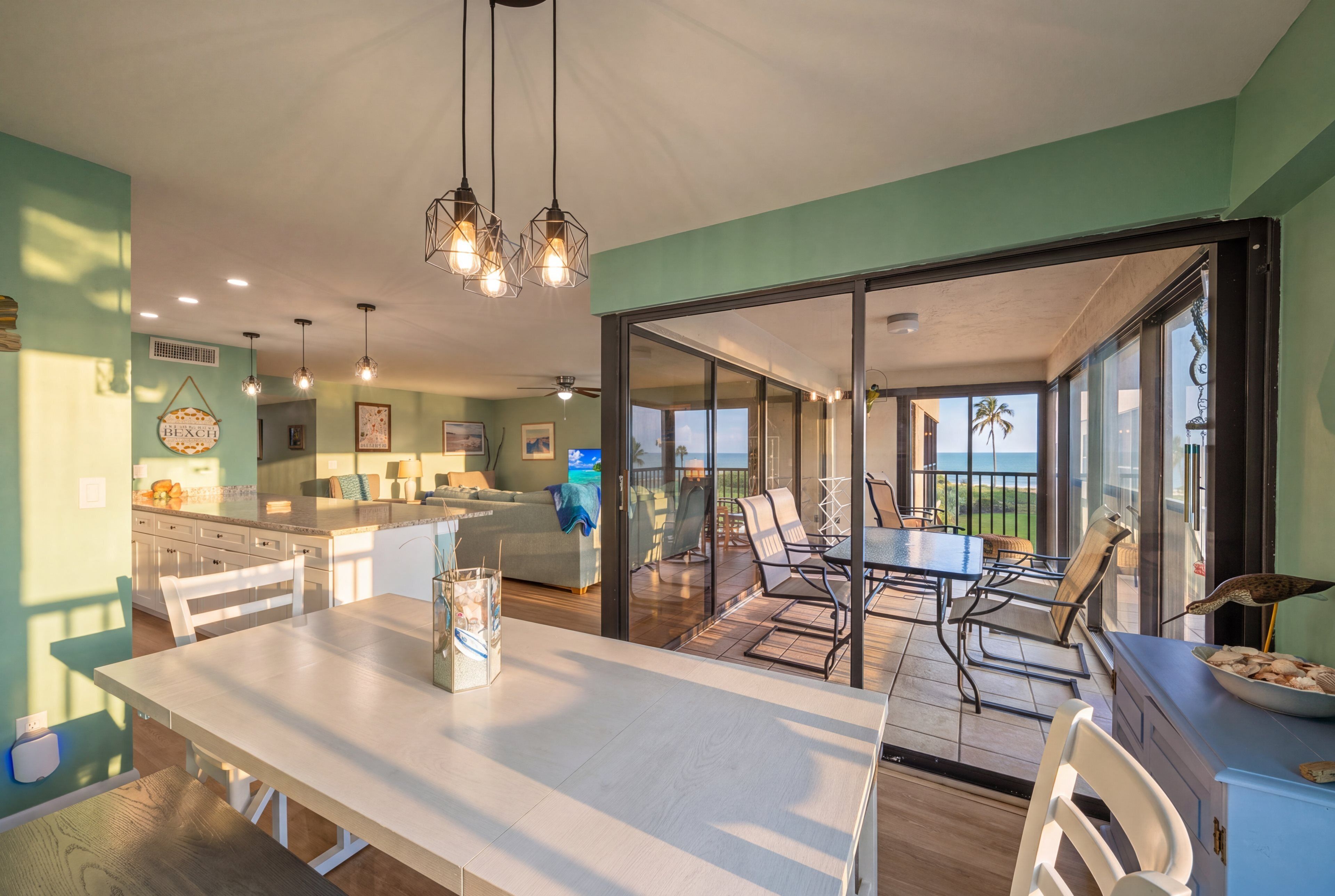 Une cuisine moderne dotée d’un îlot central, d’un coin repas avec une table et des chaises, et offrant une vue sur l’océan grâce à de grandes portes-fenêtres coulissantes.