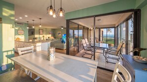 Une cuisine moderne dotée d’un îlot central, d’un coin repas avec une table et des chaises, et offrant une vue sur l’océan grâce à de grandes portes-fenêtres coulissantes.