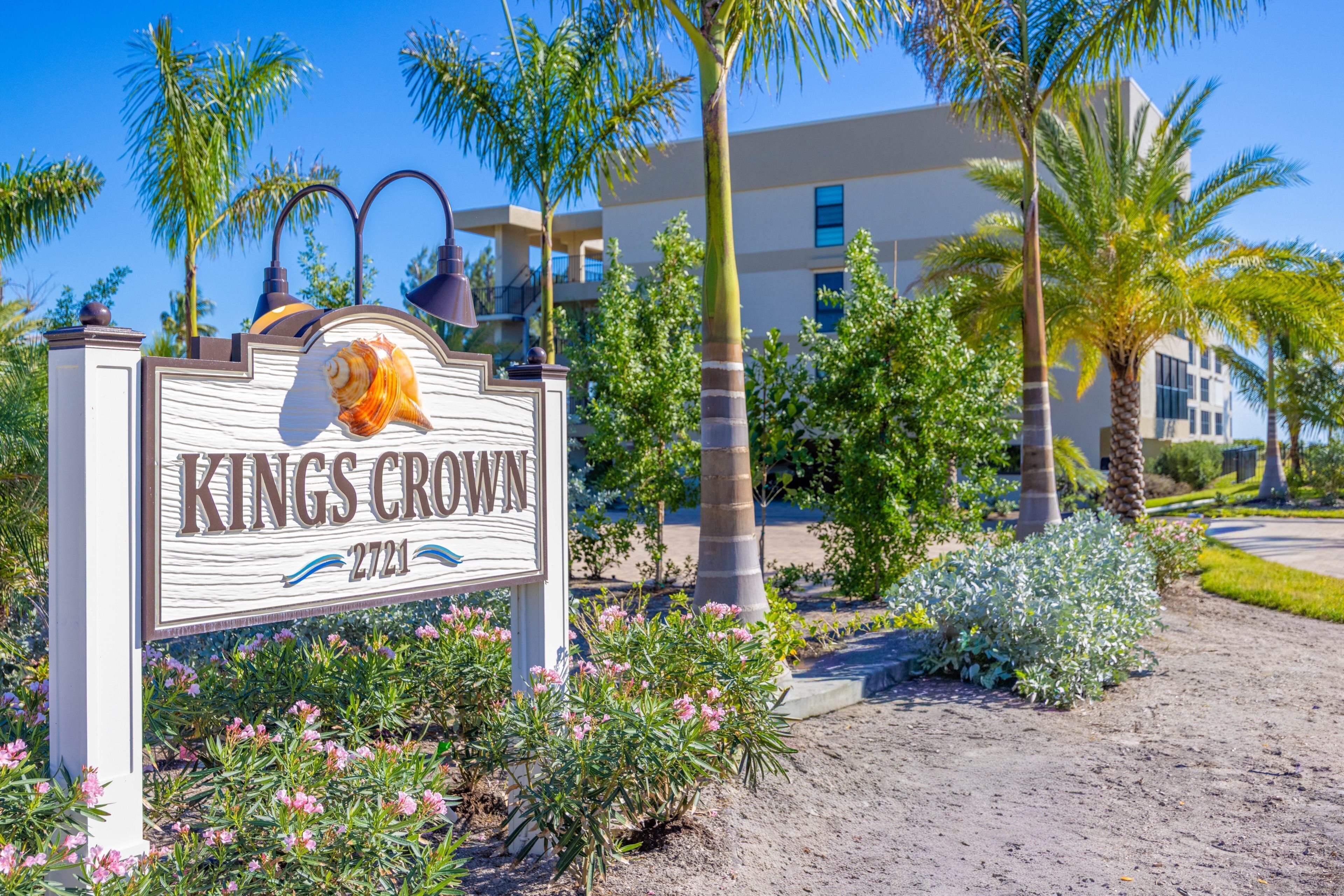 Schild für Kings Crown mit Strandmotiv, umgeben von Palmen und einem Gebäude im Hintergrund.
