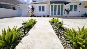 A modern two-story house with a paved driveway, potted plants, and outdoor lighting.