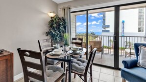 A balcony with a dining table set for two, a blue sofa, and a large potted plant.