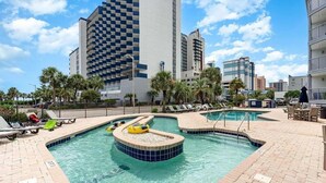 A pool area with lounge chairs, a hot tub, and a view of surrounding buildings.