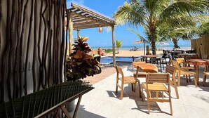 Um pátio ao ar livre com móveis de madeira, piscina e vista para a praia.