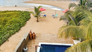 Vista da praia com área de piscina, palmeiras e cadeiras de praia.
