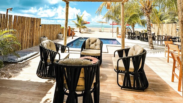 Uma área de estar externa com móveis de vime, piscina e vista para a praia.