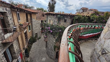 Una estrecha calle adoquinada bordeada por edificios de piedra con balcones, una cerca de hierro forjado y una bandera.