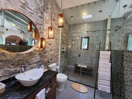 Un baño moderno con pared de piedra, un espejo grande, un lavamanos y una cabina de ducha de vidrio.