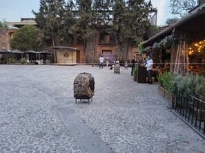 Une cour pavée de pierres, ornée d’une sculpture, avec des sièges en plein air et un bâtiment sur lequel on peut lire l’inscription « Val’Quirico ».