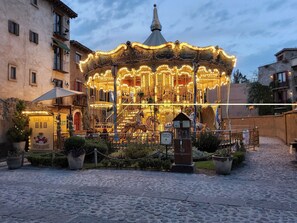 Un carrousel illuminé, entouré d’un pavé et de bâtiments.