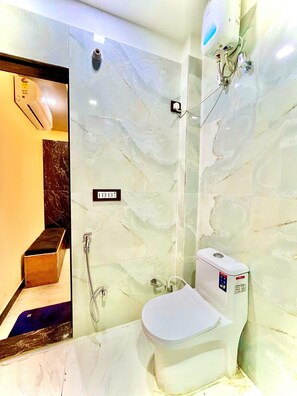 A bathroom with a marble wall, a toilet, a shower, and a hand dryer. - YS TAJ HOTEL AGRA (Agra)