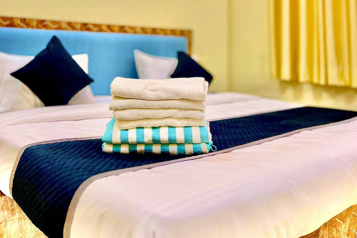 Une chambre d’hôtel avec un lit bien fait, une pile d’serviettes et une fenêtre avec des rideaux.