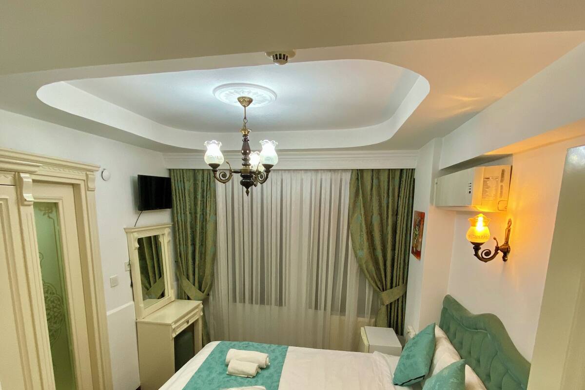A hotel room with a bed, a chandelier, a television, and a wall-mounted lamp.