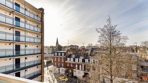 Een meerhoog gebouw met balkons, een parkeerplaats en omliggende, oudere gebouwen.