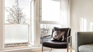 Een moderne woonkamer met een groot raam, een lederen fauteuil en een grijze bank.