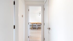 Een smalle gang die uitkomt in een kamer met een bed, een houten tafel en een stoel.