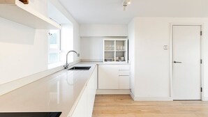Een moderne keuken met witte kastjes, een inbouwspoelbak en een raam dat voor natuurlijk licht zorgt.