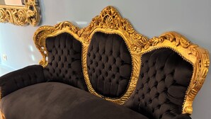 A black sofa with gold trim and tufted backrests, positioned against a light blue wall. - Le Mini Versailles (Goussainville)